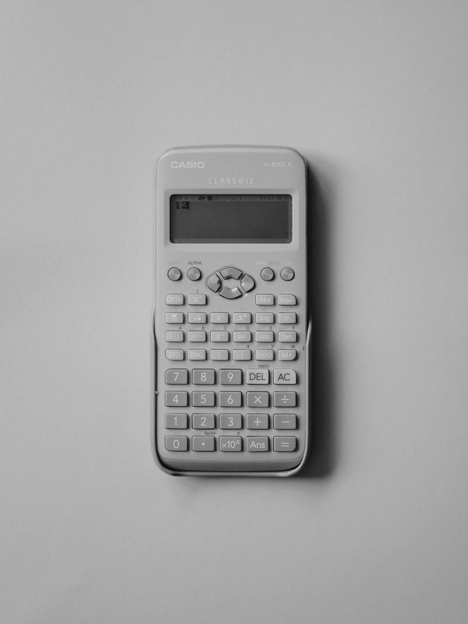 A white calculator lying on a grey surface.