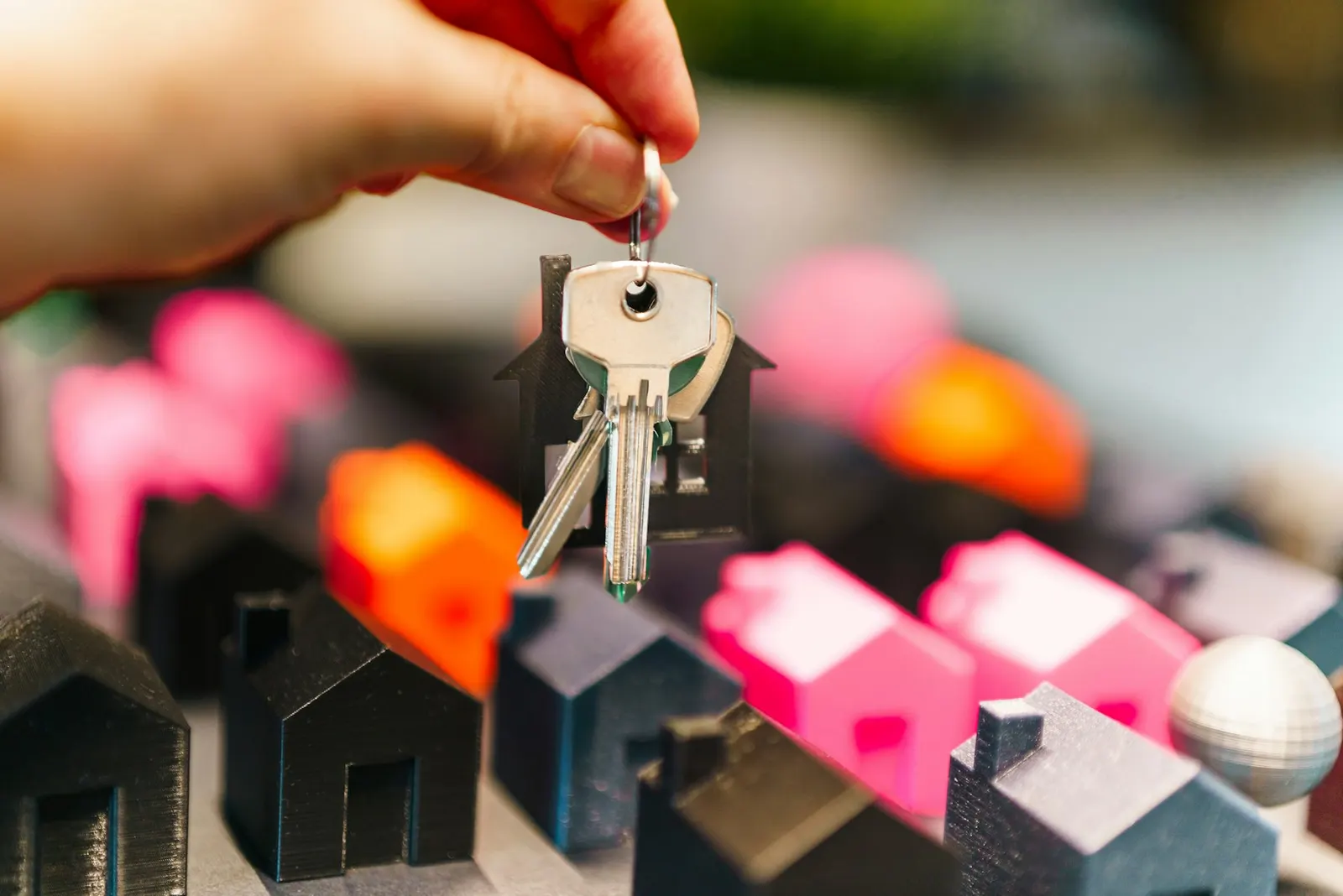 A hand holding a set of house keys above small toy houses.