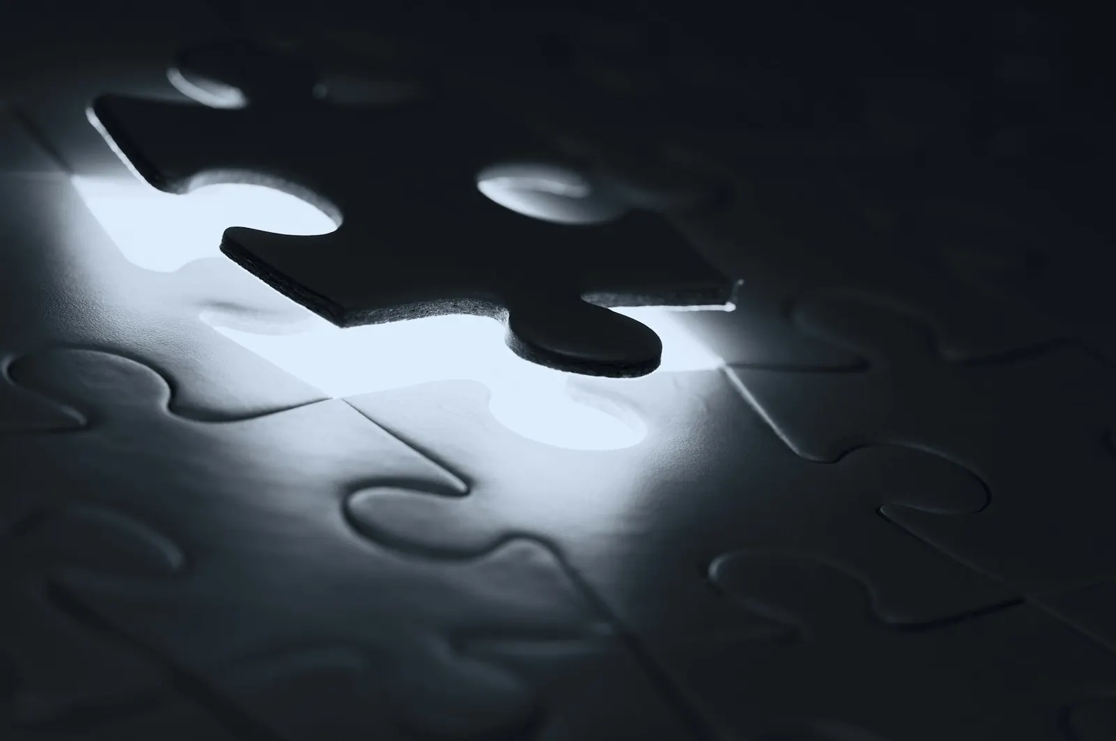 A dark jigsaw puzzle with one piece lifted out, lit from below.