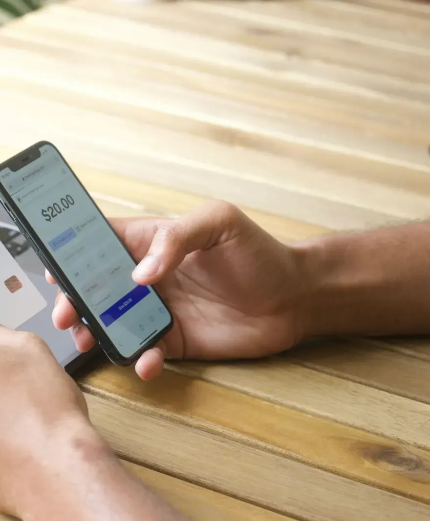 A hand holding a phone that shows a $20.00 payment, with a payment card in the other hand.
