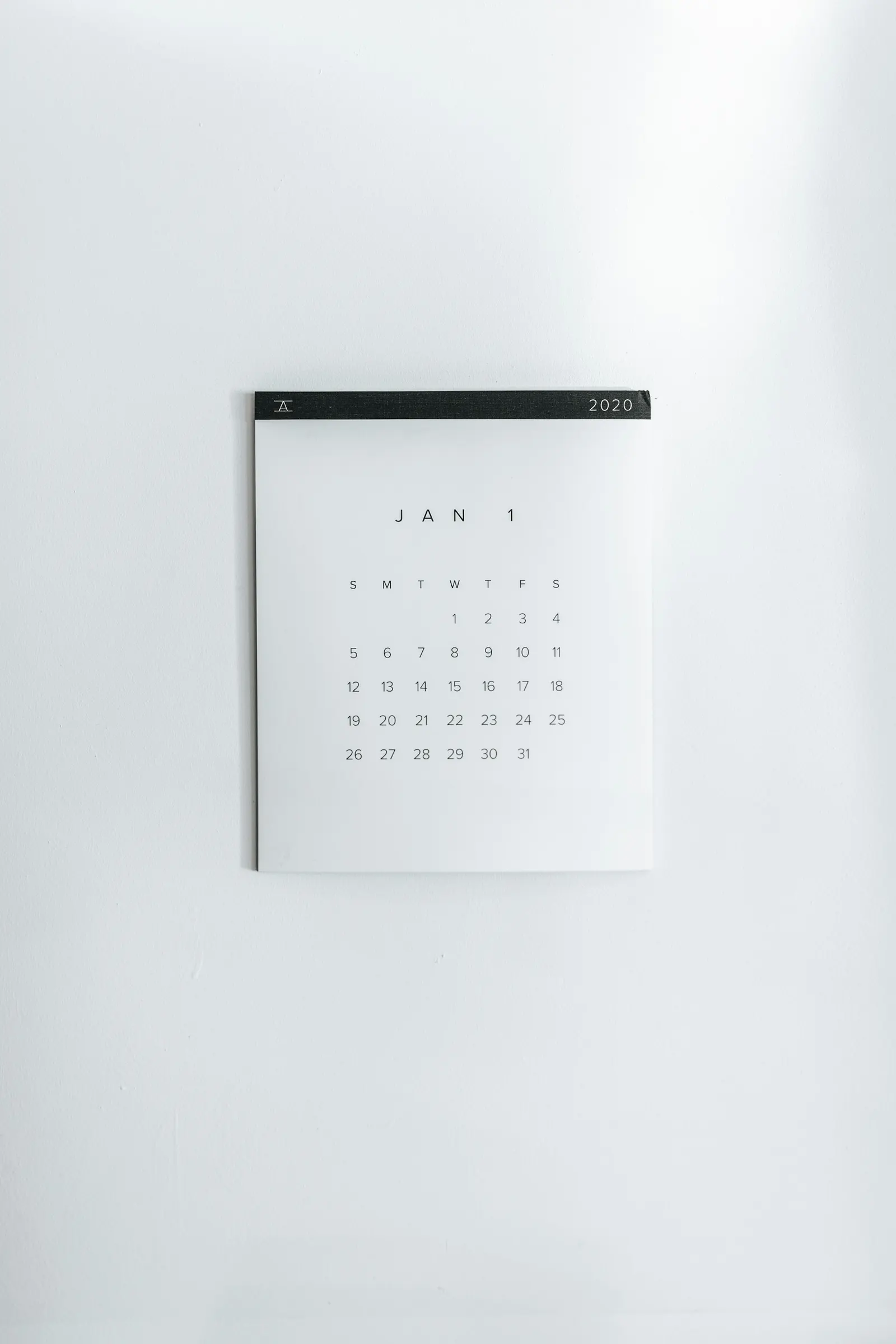 A white wall calendar for January hanging on a plain white wall.