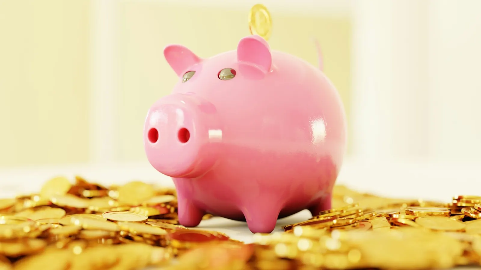 A pink piggy bank standing on a pile of gold coins, with one coin falling into the slot.