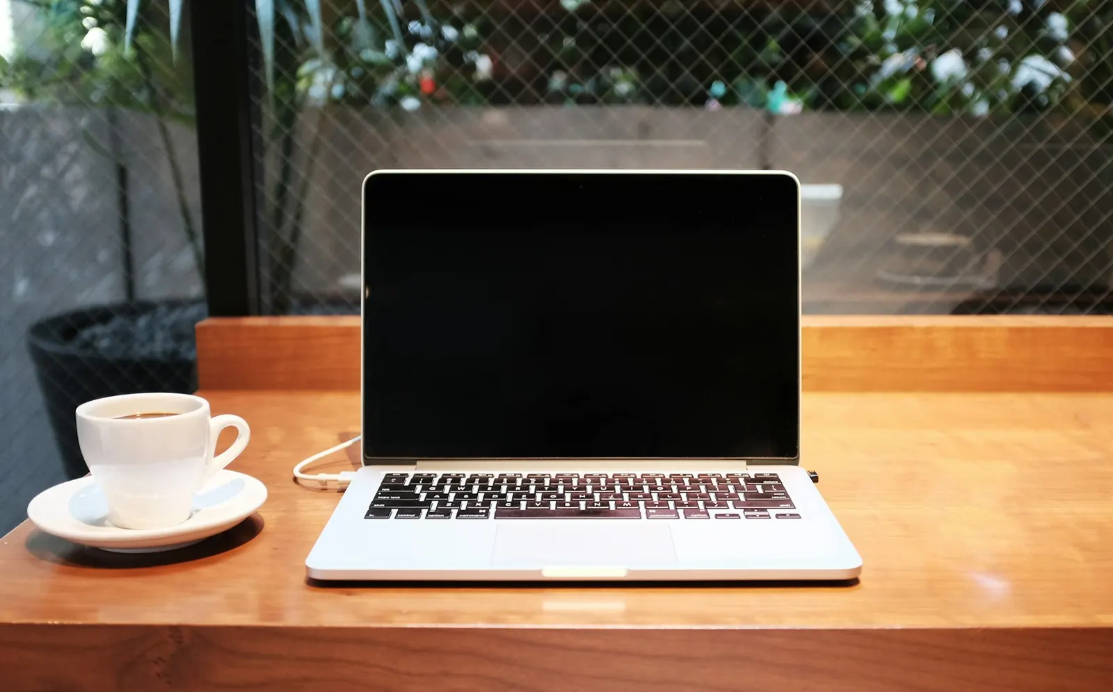 An open laptop on a wooden desk, next to a cup of coffee.