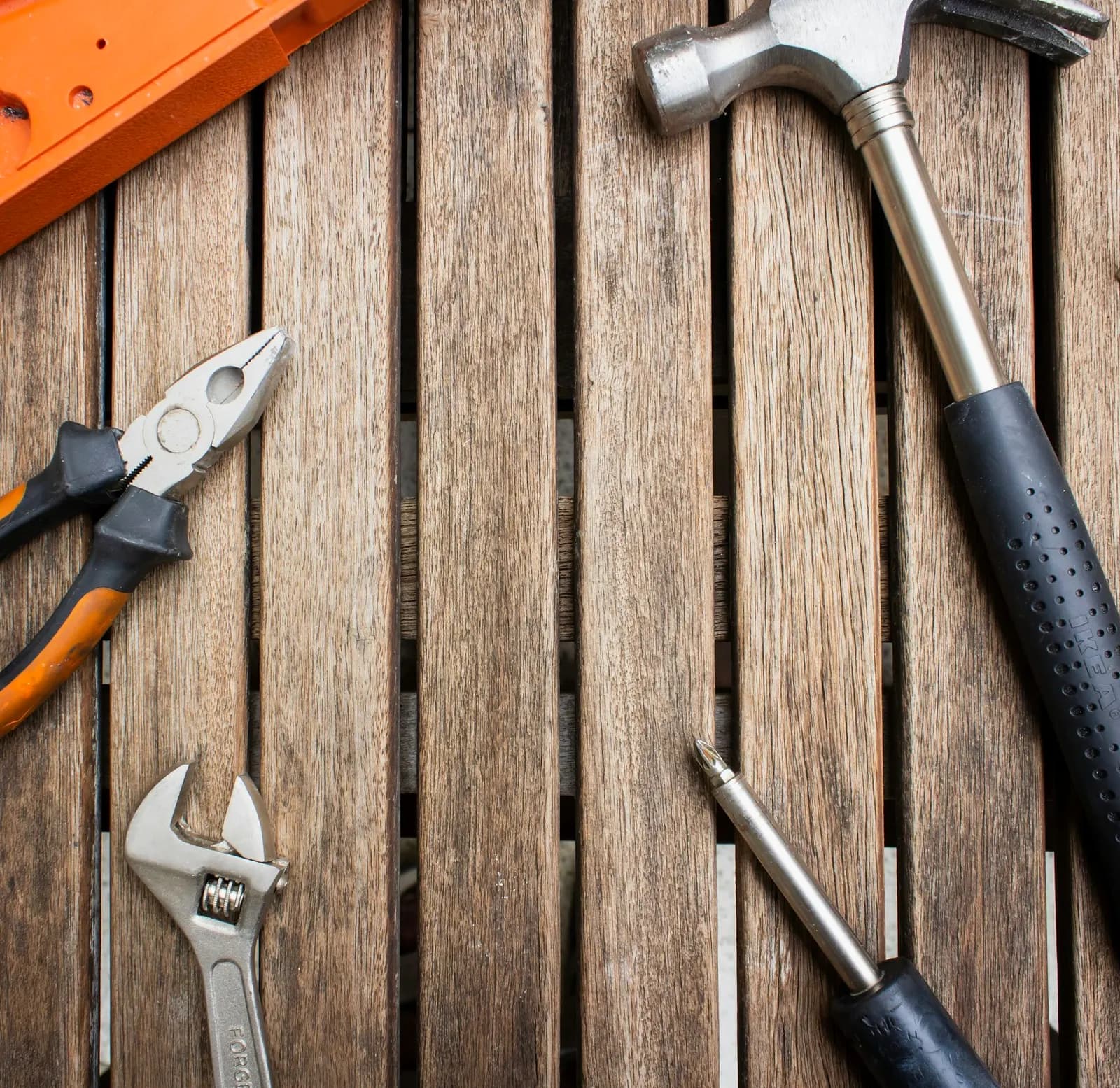 Pliers, a wrench and a screwdriver arranged on a wooden table.
