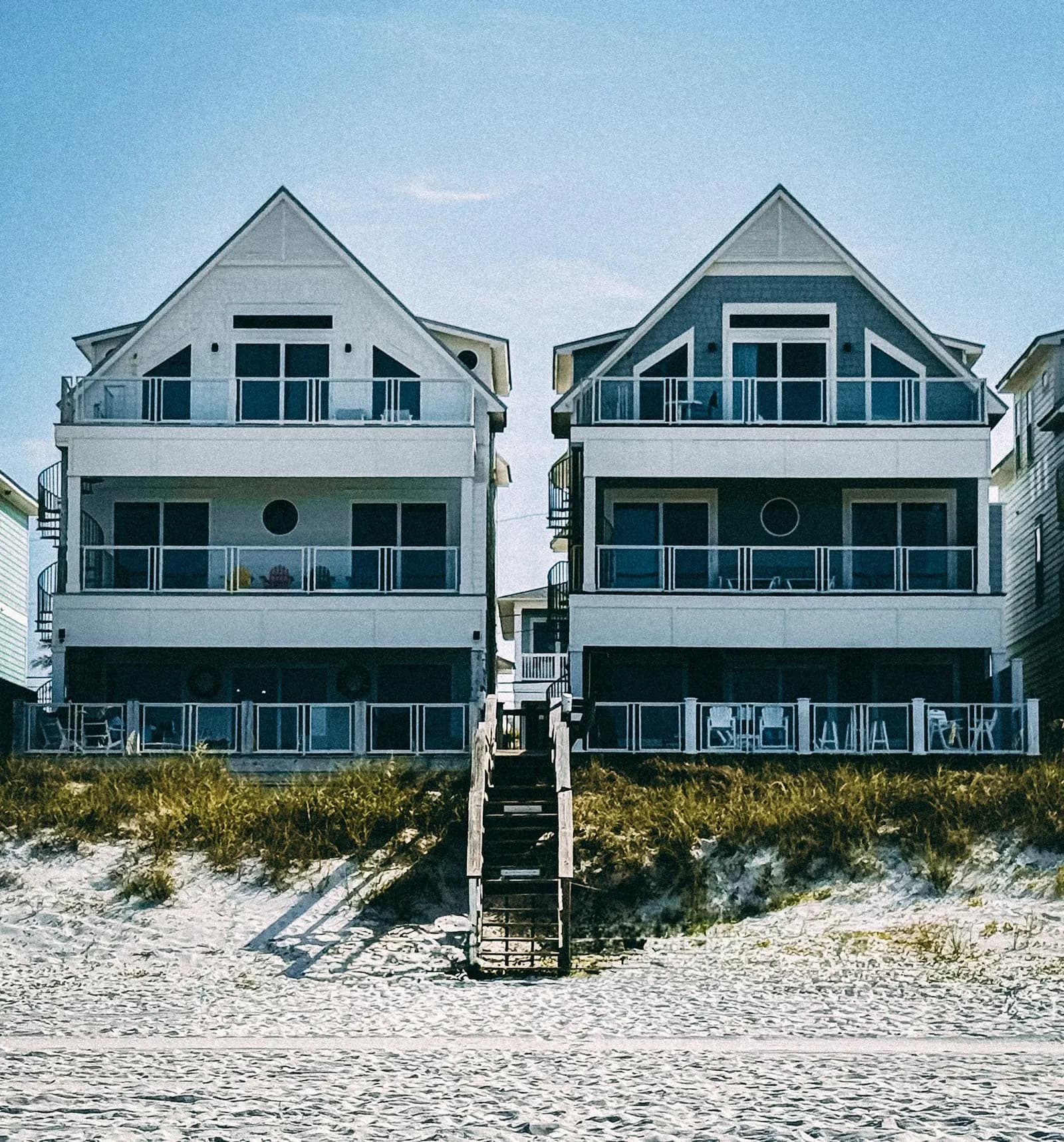 Two modern beach houses with stairs leading down to the sand.