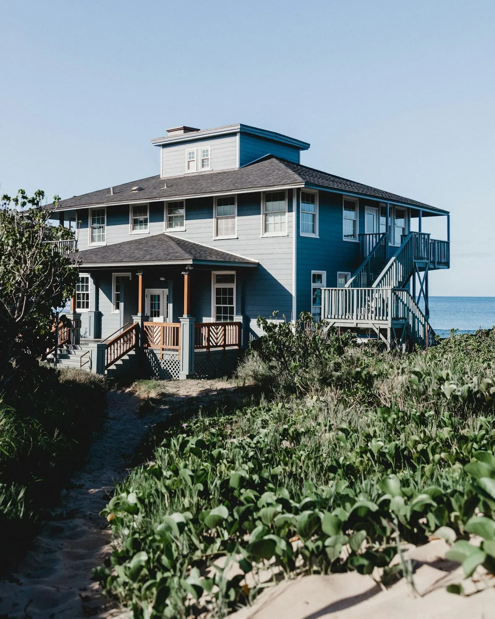 A blue and white beach house with a covered porch and a sandy path.