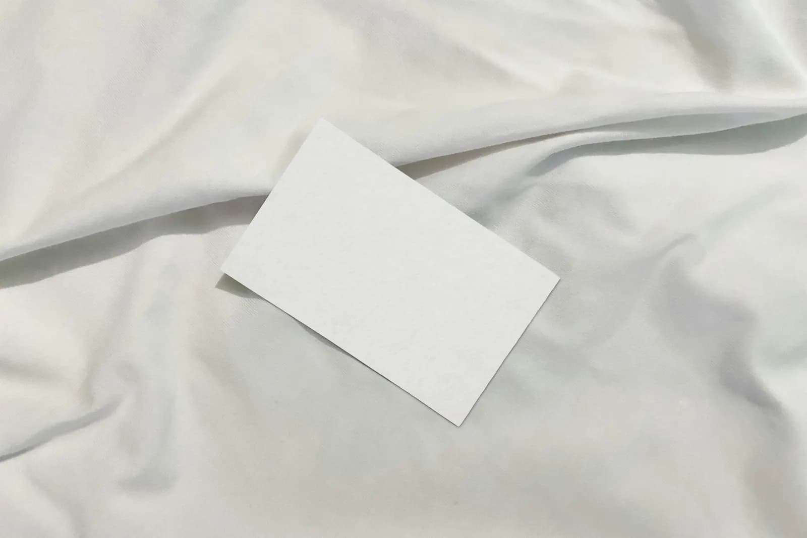 A blank white card lying on crumpled white bed linen.
