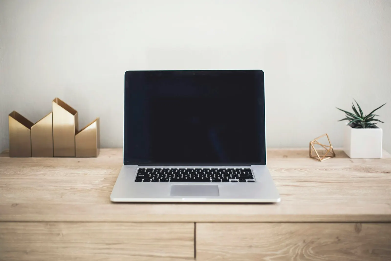 A laptop on a light wooden desk in a bright room.