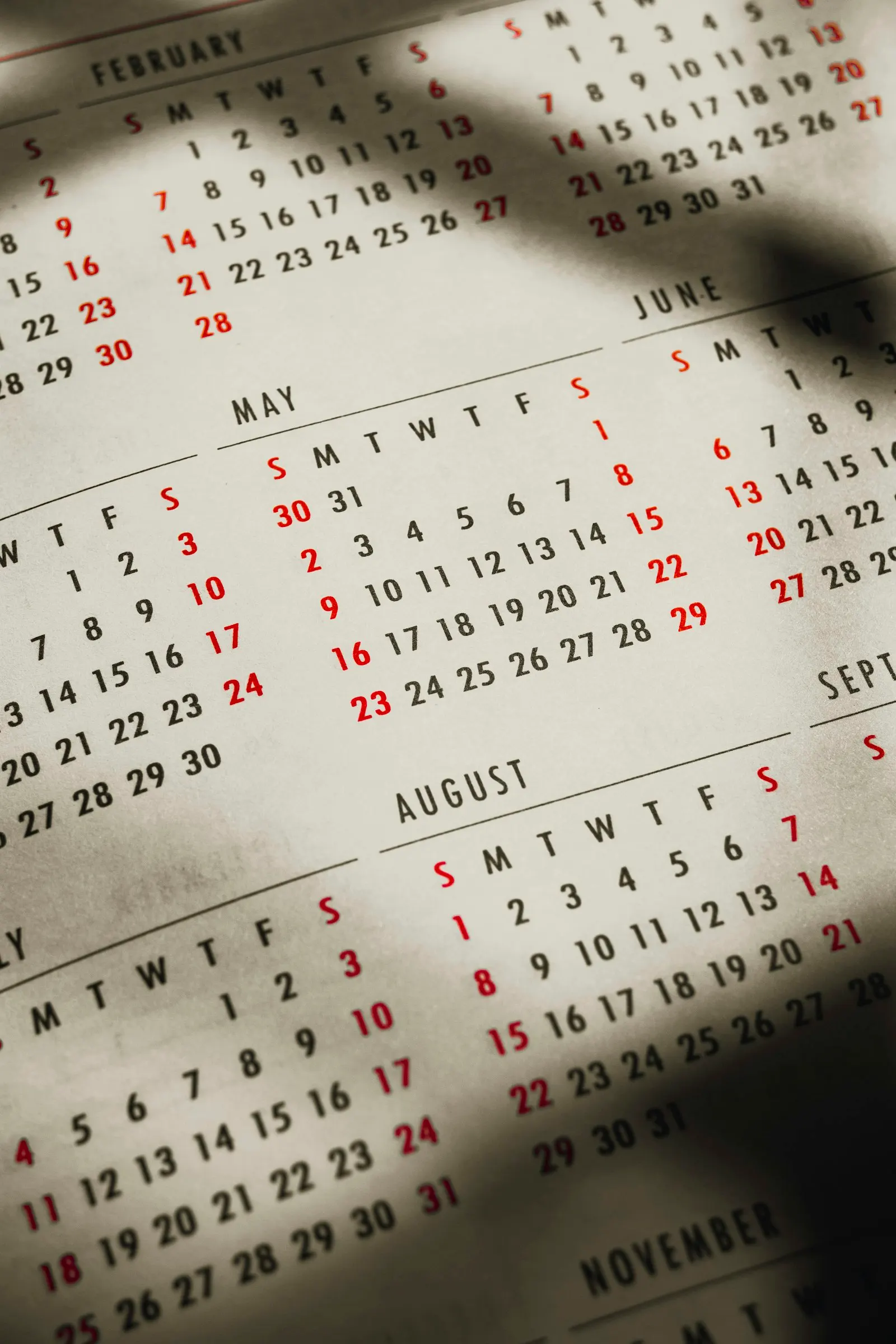 A close-up of a printed wall calendar showing several months, with weekends marked in red.